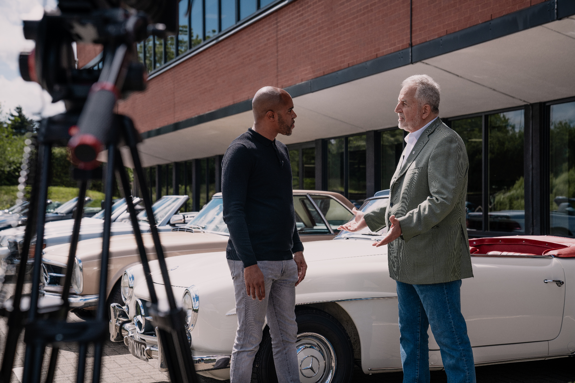 Shaun Benn interviewing a guest in front of classic Mercedes-Benz cars during a filmed feature